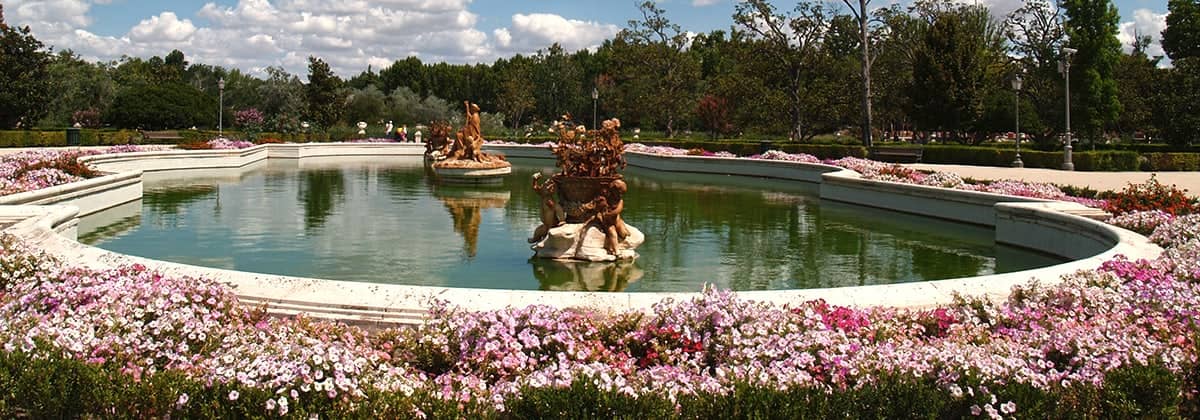 Un estanque con esculturas y macizos de flores en un jardín de Aranjuez.